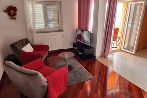 A living room with a sofa, a television, and a window with blinds. - De Lux 4-Star Apartment with Ocean View, Rabac, Croatia (Rabac)