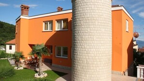 En modern byggnad med en cylindrisk struktur av tegel, orange väggar och en välskött trädgård med palmer.