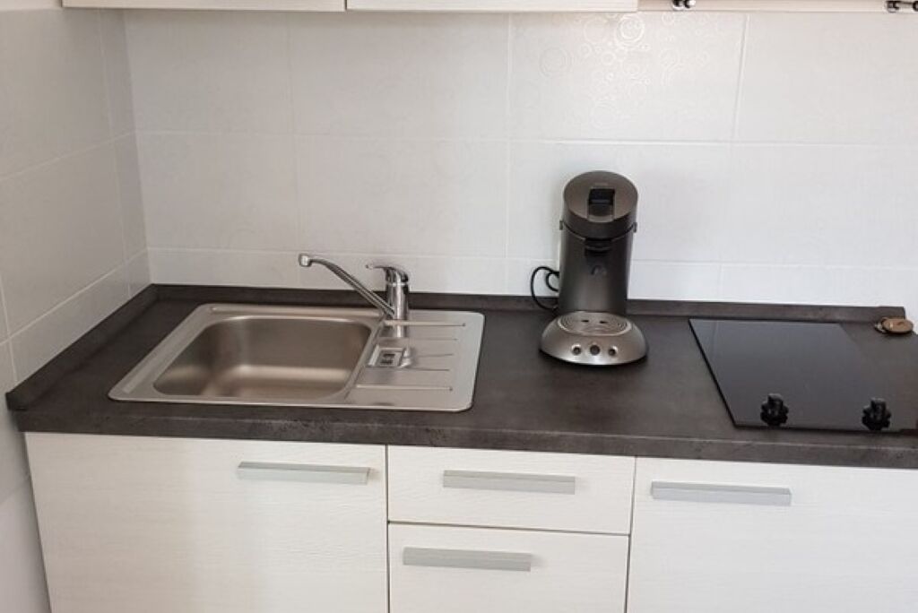 A kitchen with a stainless steel sink, a coffee maker, and a black cutting board on the countertop.