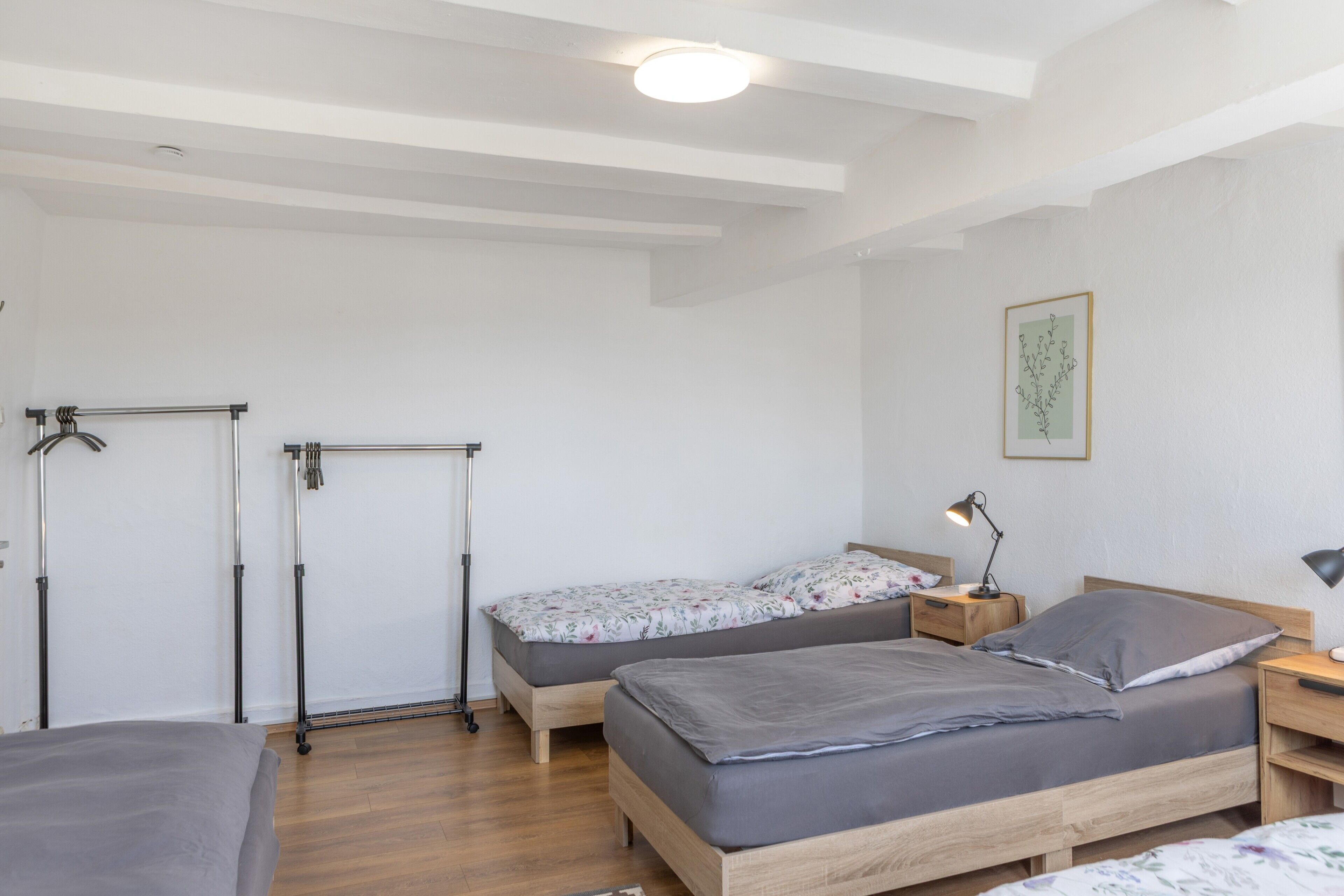 Ein Schlafzimmer mit zwei Betten, Holzboden, Wandheizkörper und einem Nachttisch mit Lampe.