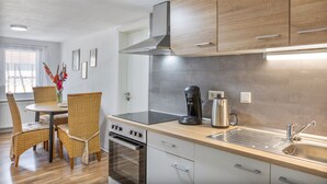 Una cocina moderna con armarios de madera, estufa de acero inoxidable, horno empotrado, cafetera y pileta.