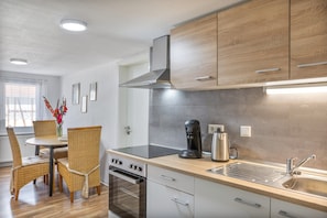 A modern kitchen with wooden cabinets, a stainless steel range, a built-in oven, a coffee maker, and a sink. - Apartment Fewo50 – bis 7 Personen, 2 Schlafzimmer/2 Bäder ab 4 Personen (Homberg (Efze))