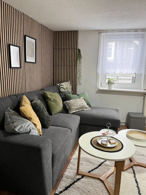 A modern living room with a grey sectional sofa, a round coffee table, and a window with sheer curtains. - Apartment 'Fewo50' 2 Bedrooms/2 Bathrooms – No Terrace (Homberg (Efze))