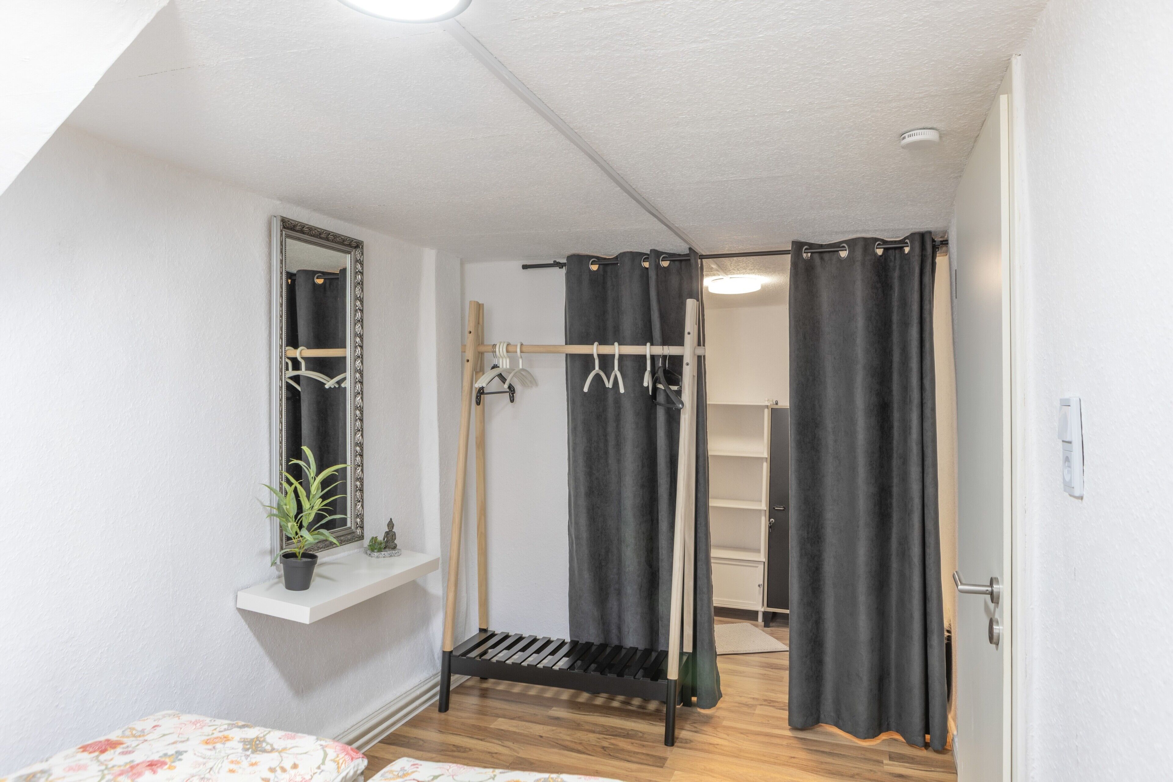 Een knus slaapkamer met een bed, een kamerplantje, een spiegel, een kledingkast en een douche.