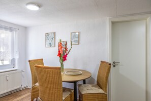 A dining area with a round table, four wicker chairs, a vase with flowers, and two framed pictures on the wall. - Apartment 'Fewo50 - bis 7 Personen, 2 Schlafzimmer/2 Bäder ab 4 Personen' (Homberg (Efze))