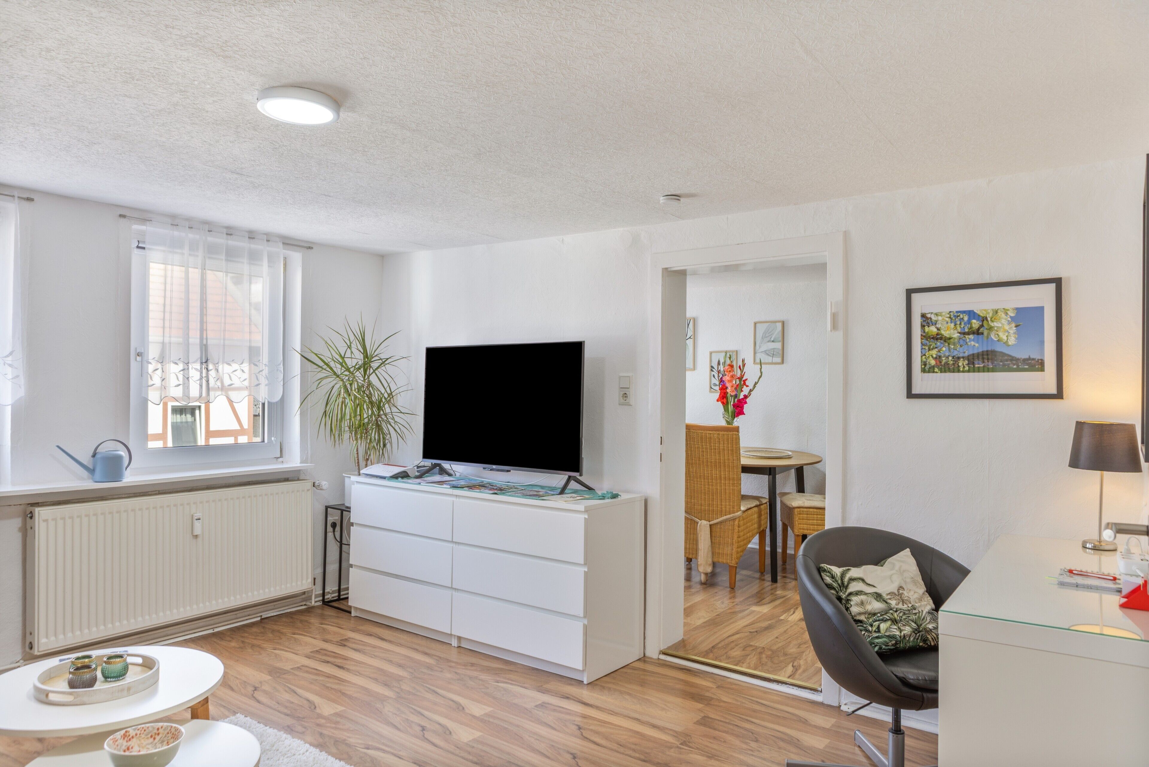A modern living room with a flat-screen TV, a dining area with a table and chairs, and a small seating area with a chair and a sofa.