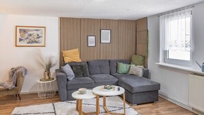 Una sala de estar moderna con un sofá seccional gris, dos mesas redondas, un jarrón decorativo y una ventana con cortinas de gasa.