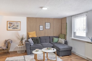 A modern living room with a grey sectional sofa, two round tables, a decorative vase, and a window with sheer curtains. - Apartment Fewo50 – bis 7 Personen, 2 Schlafzimmer/2 Bäder ab 4 Personen (Homberg (Efze))