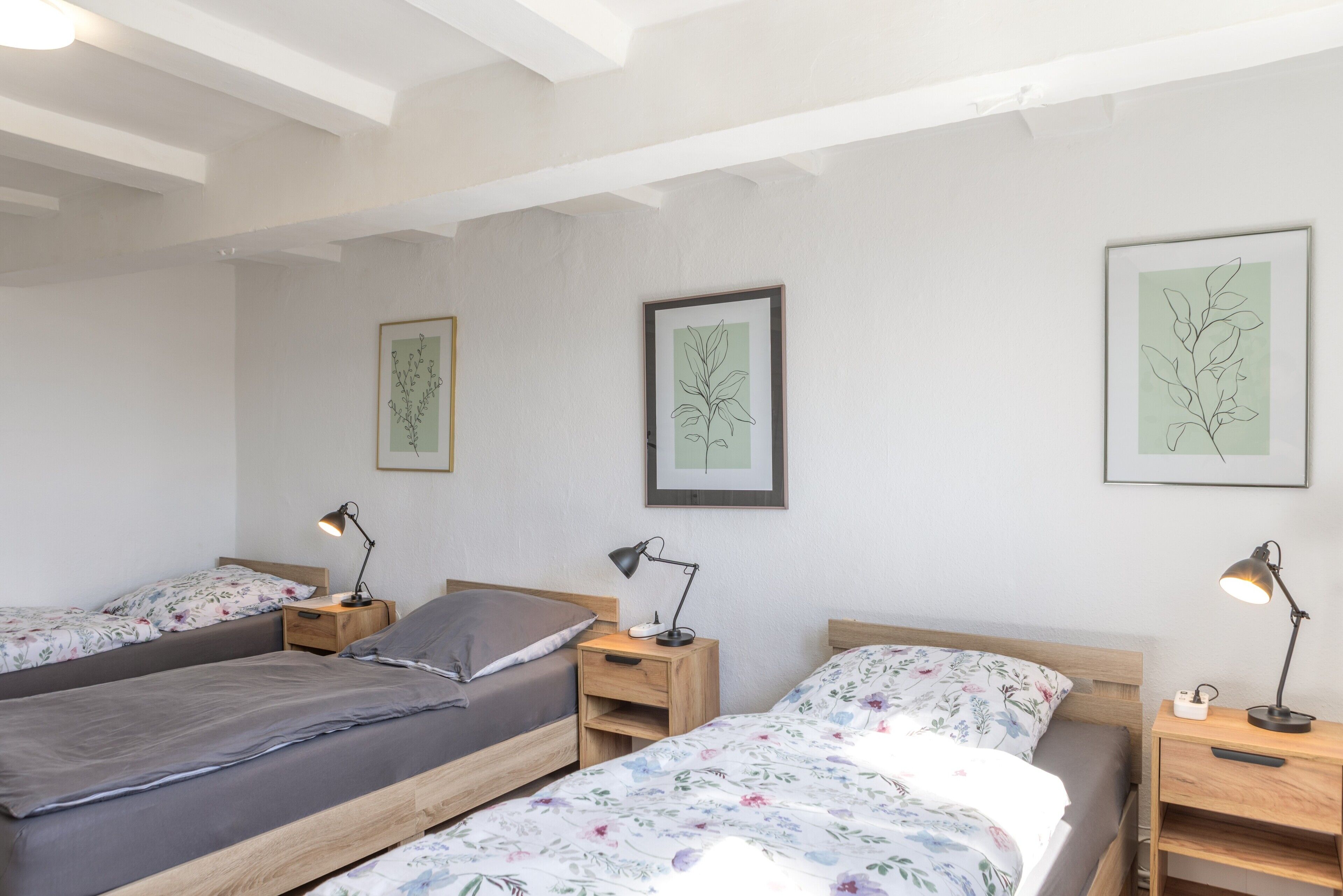Une chambre avec deux lits, chacun doté d’une table de chevet et d’une lampe de bureau. Les murs sont ornés d’illustrations botaniques encadrées.