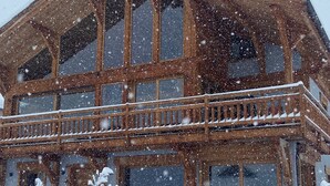 Ein großes Holzgebäude mit zahlreichen Fenstern und einem Balkon. Es schneit draußen.