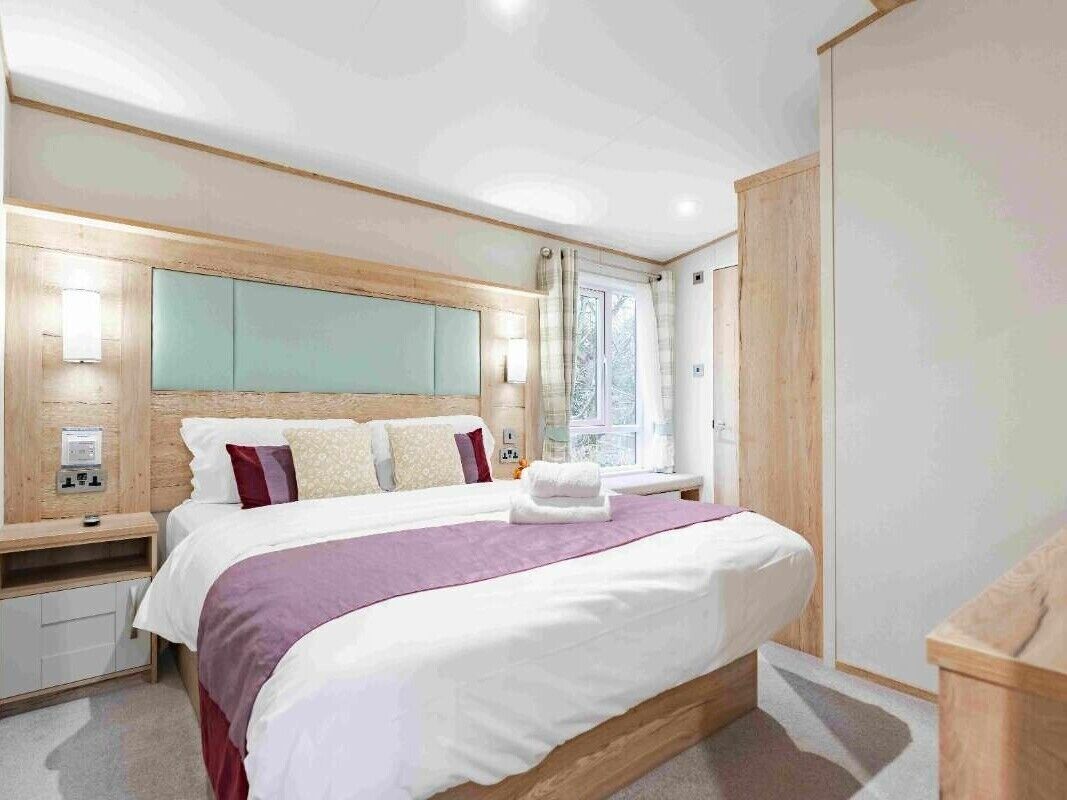 Un dormitorio moderno con una cama grande, cabecera de madera, mesitas de noche y una ventana con cortinas.