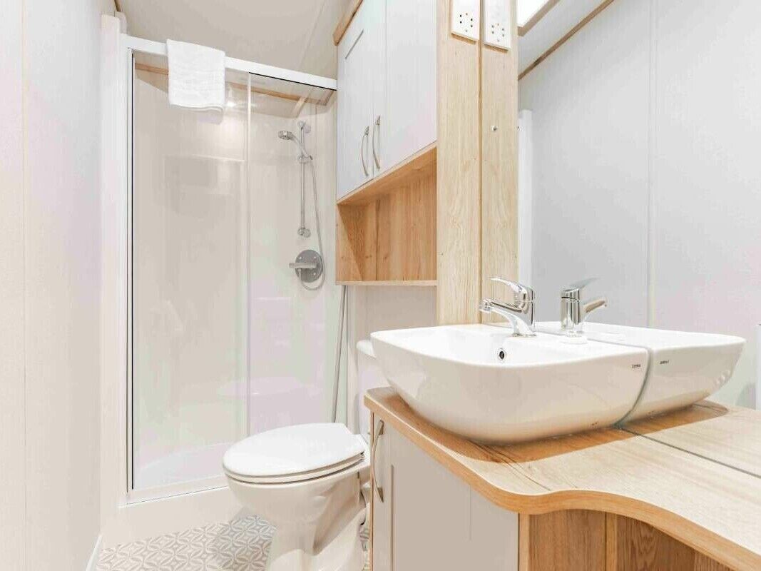 Et moderne badeværelse med en glasafskærmet brusekabine, et hvidt toilet og en trækommode med en stor vask.