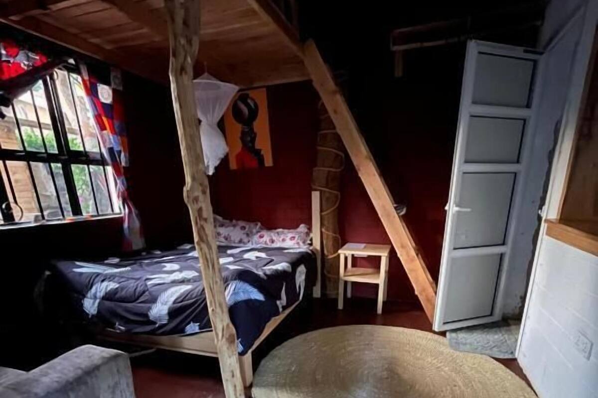 A rustic room with a loft bed, a small wooden chair, a woven mat on the floor, and a white wardrobe.