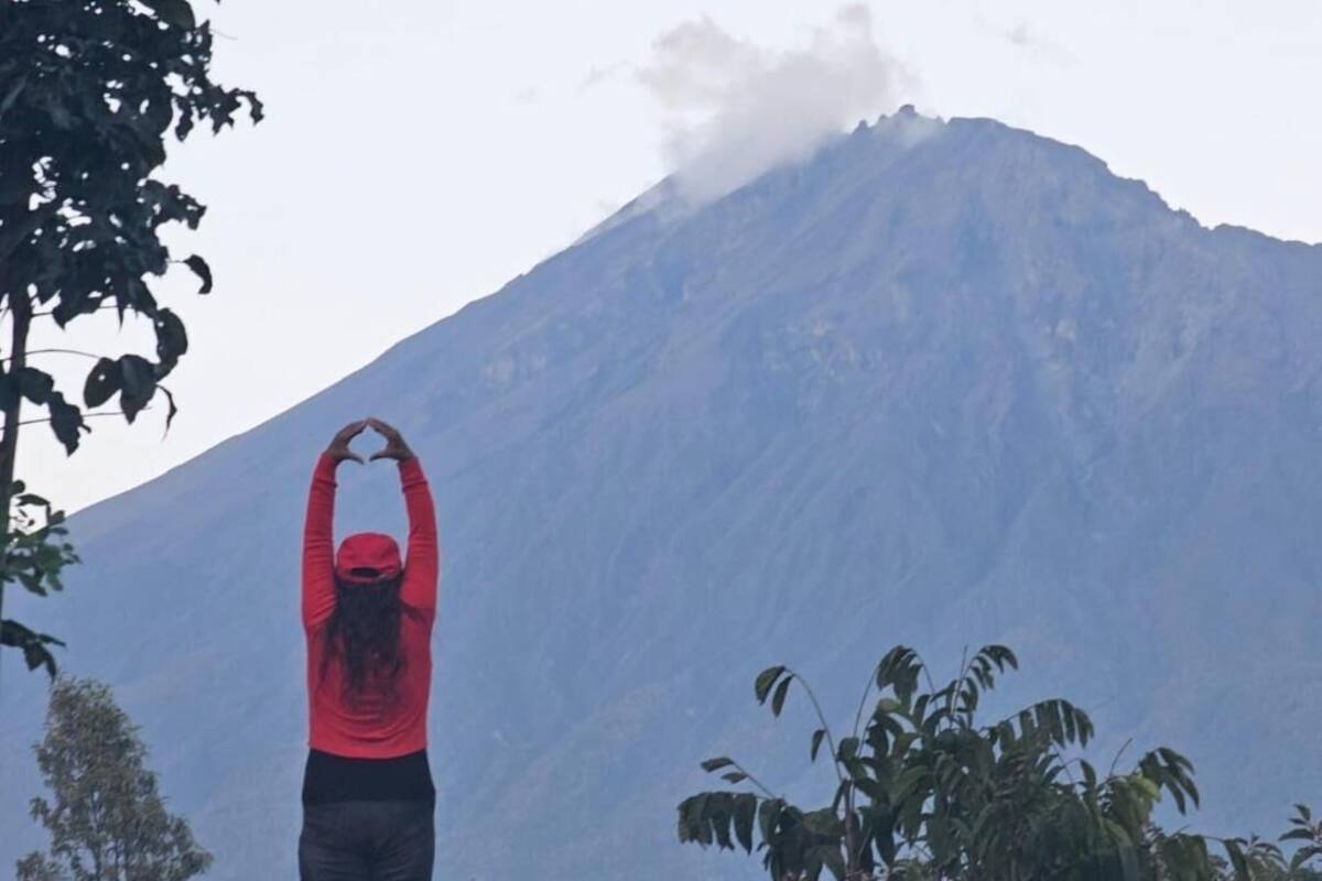 A person standing with arms raised in front of a mountain.