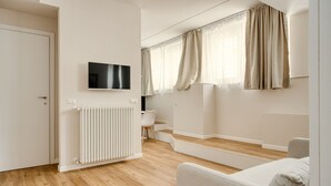 A modern living room with a flat-screen TV, a radiator, a sofa, and a window with curtains. - Hostmate - Milano - Imperia's Warm - Romolo IULM (Milano)
