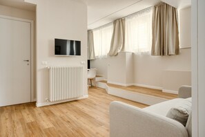 A modern living room with a flat-screen TV, a radiator, a sofa, and a window with curtains. - Hostmate - Milano - Imperia's Warm - Romolo IULM (Milano)