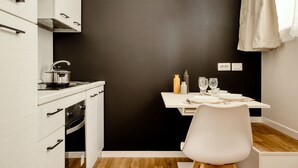 A compact kitchen with white cabinetry, a stove, and a dining area with a table set for two. - Hostmate - Milano - Imperia's Warm - Romolo IULM (Milano)