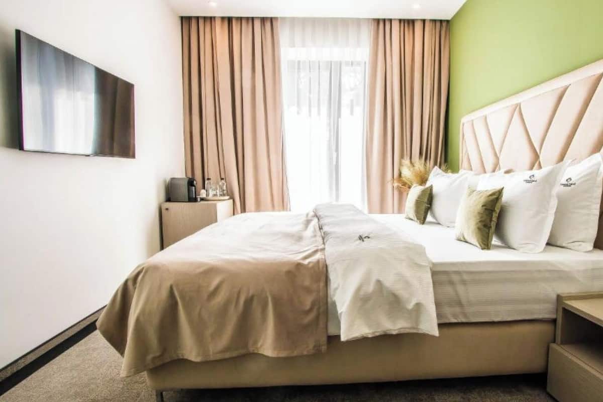 Una habitación de hotel con cama, mesitas de noche, televisión y cortinas.