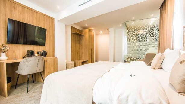 A modern hotel room with a large bed, a desk with a chair, a flat-screen TV mounted on the wall, and a glass partition with a decorative pattern. - Central Carol APARTHOTEL (Bucharest)