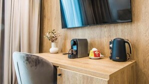 A hotel room with a wooden desk, a flat-screen TV mounted on the wall, a coffee maker, a kettle, a vase with dried flowers, and a chair. - Central Carol APARTHOTEL (Bucharest)