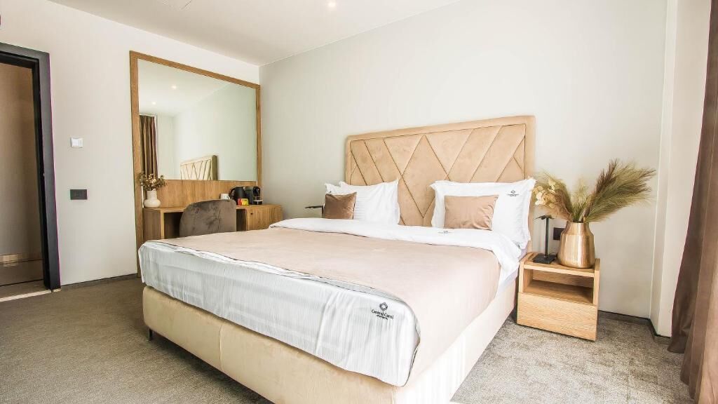 Une chambre d’hôtel avec un grand lit, une tête de lit en bois, une table de chevet avec une lampe et un miroir au mur.