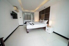 A modern hotel room with a large bed, a bedside table with a lamp, a TV mounted on the wall, and a bathroom visible through a glass door. - Wonderland Amethyst Luxury Villa (Muang Pattaya)