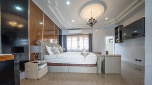 A modern hotel room with a large bed, a bedside table, a chair, a TV, and a chandelier. - Wonderland Amethyst Luxury Villa (Muang Pattaya)