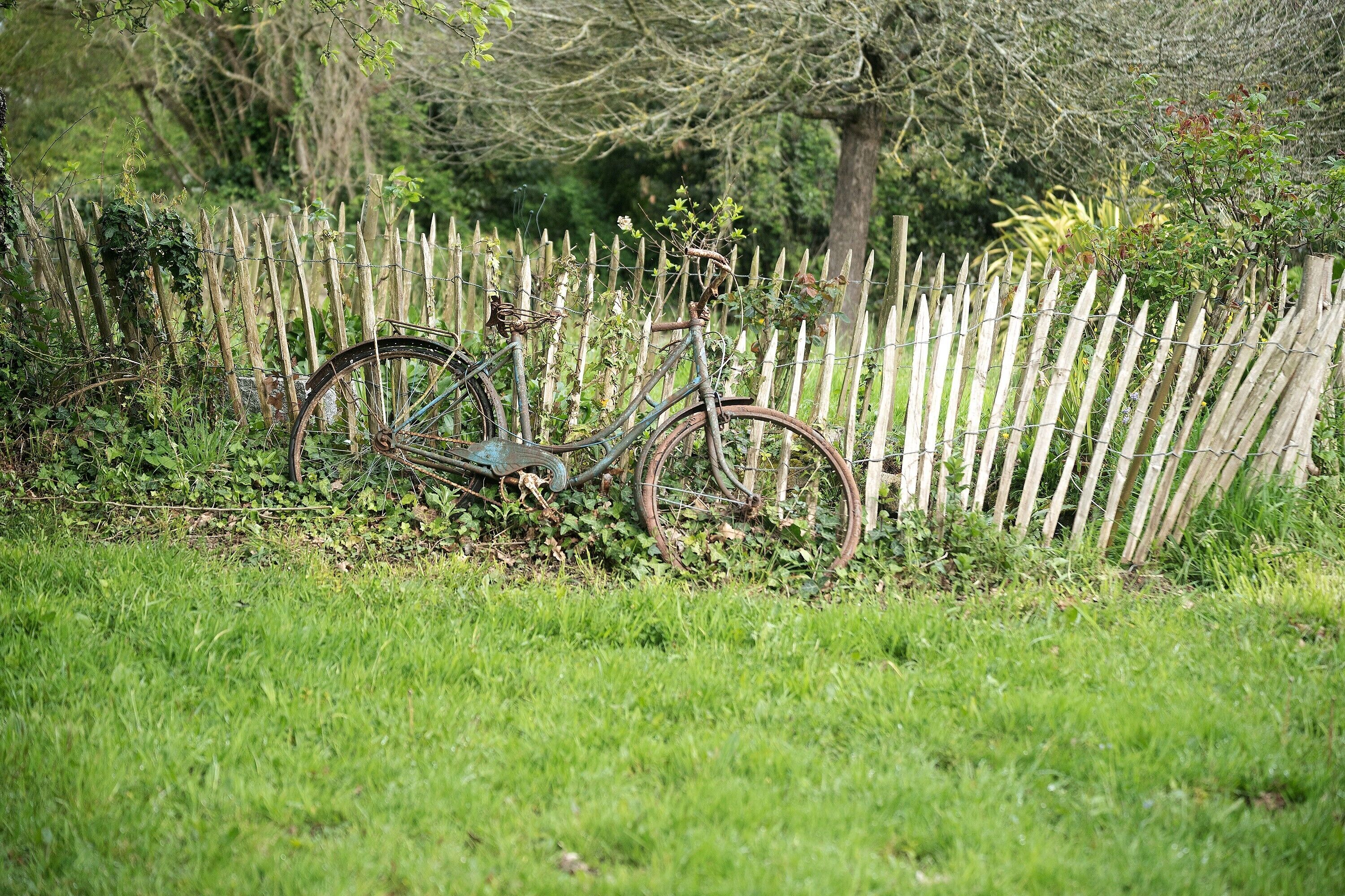 Una bicicleta apoyada en una valla de madera en una zona con césped.