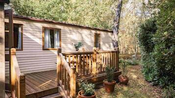 A wooden cabin with a deck, surrounded by trees and potted plants.