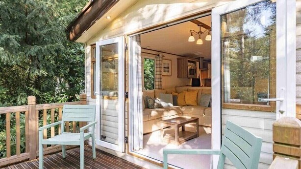 Een gezellig chalet met een houten terras, een bank en een eettafel.