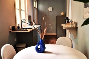 A dining area with a round table, chairs, a blue vase with decorative elements, a clock on the wall, and a kitchen area in the background. - Apt. Presidencial - Historic Mansion with Patio, Terrace & Garden View (La Orotava)