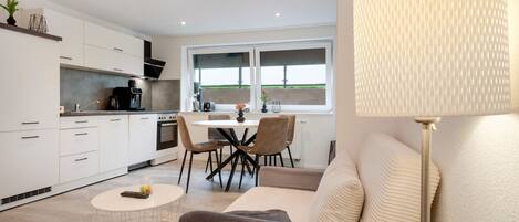 A modern kitchen with white cabinets, a dining area with a table and chairs, and a sofa with a lamp.
