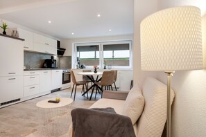 A modern kitchen with white cabinets, a dining area with a table and chairs, and a sofa with a lamp.