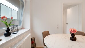 Ein Essbereich mit einem runden Tisch, Stühlen, einem Fenster mit Blumen und einer Tür.