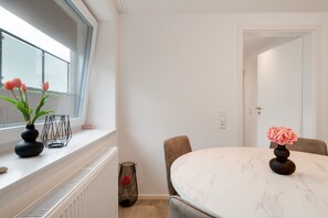Un coin repas avec une table ronde, des chaises, une fenêtre décorée de fleurs et une porte.