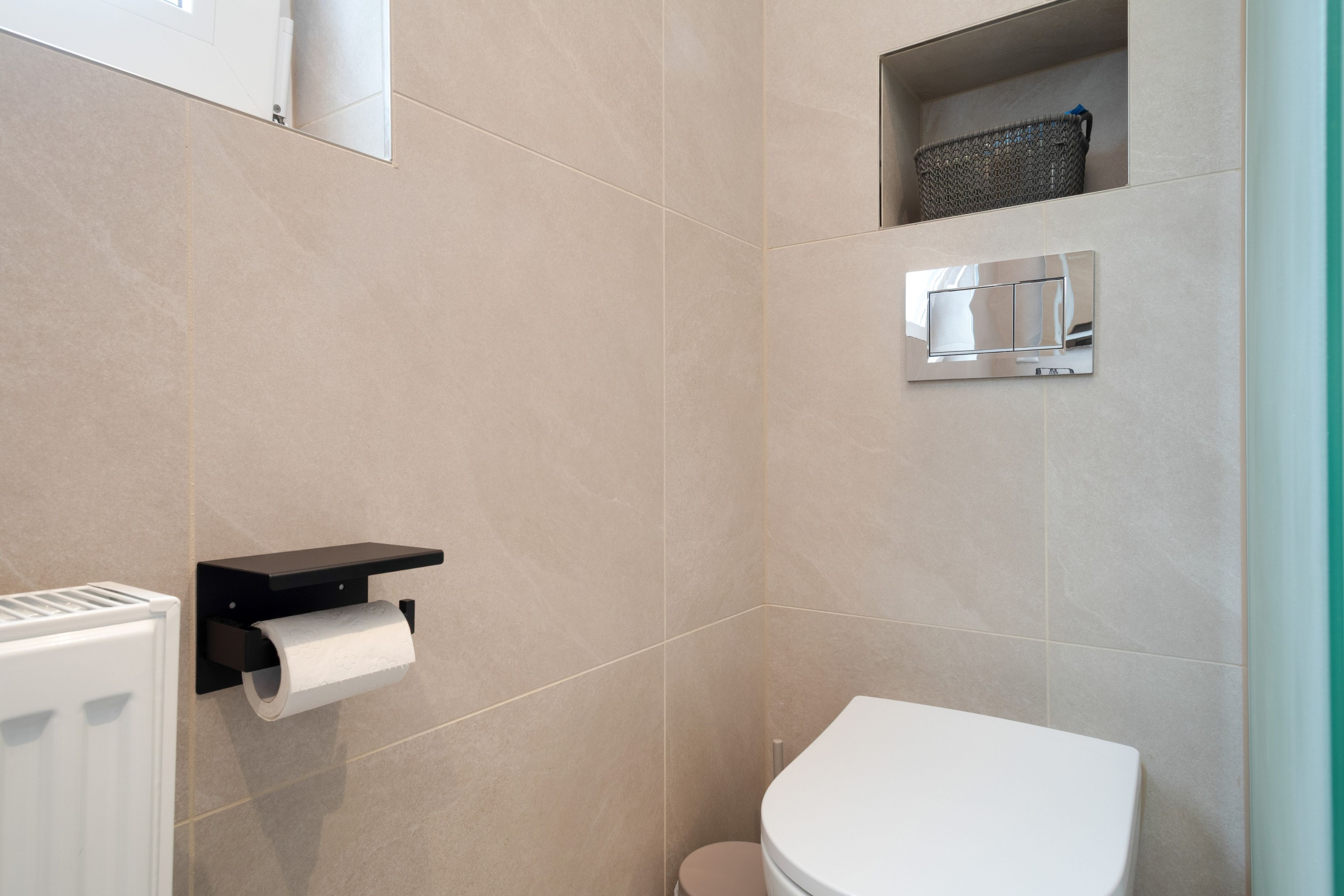 Une salle de bain équipée de toilettes, d’un distributeur de serviettes et d’une petite étagère avec un panier.