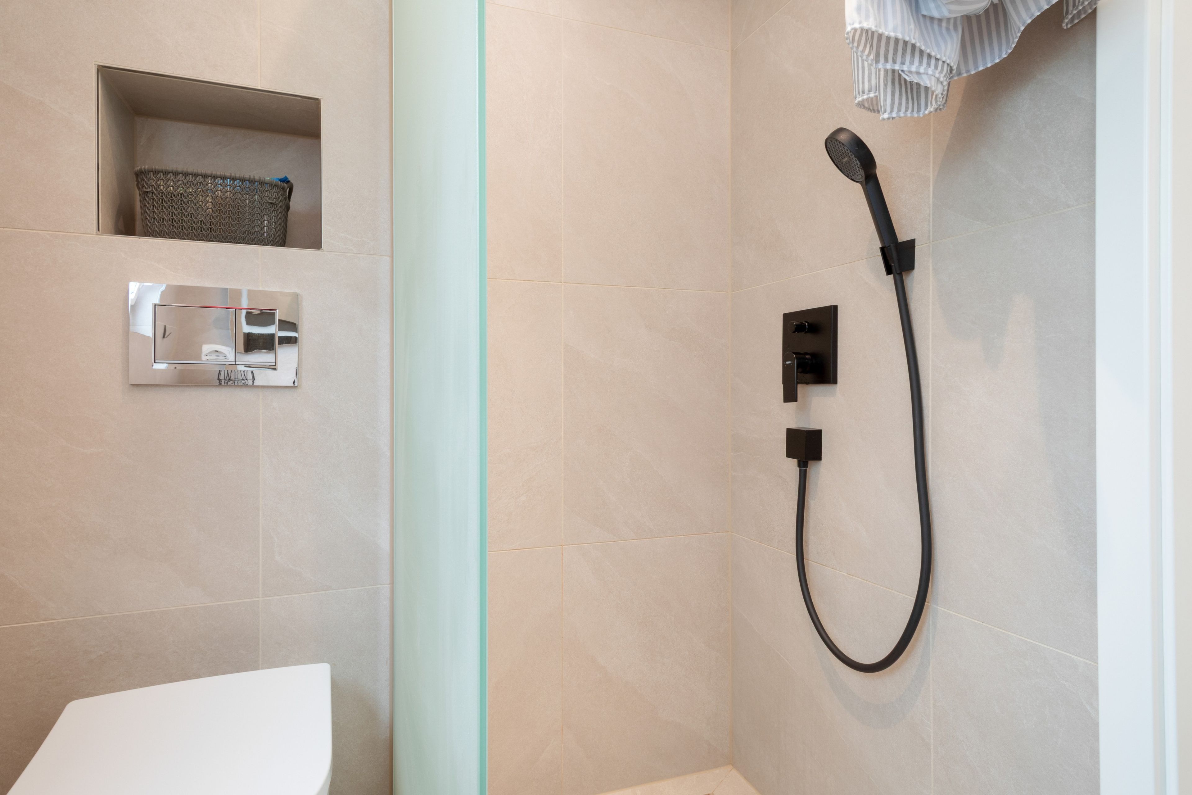 Ein Badezimmer mit Toilette, einer Dusche inklusive Handbrause und einem Handtuchhalter.