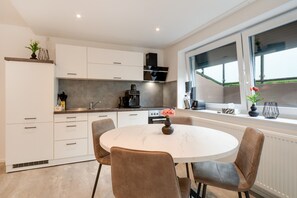A modern kitchen with white cabinets, a coffee machine, and a dining area with a round table and chairs.