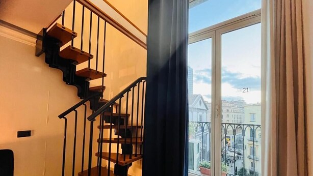 A staircase with wooden steps and black railings, leading to a balcony with a view of buildings and a ship in the distance. - Parthenope b&b (Naples)