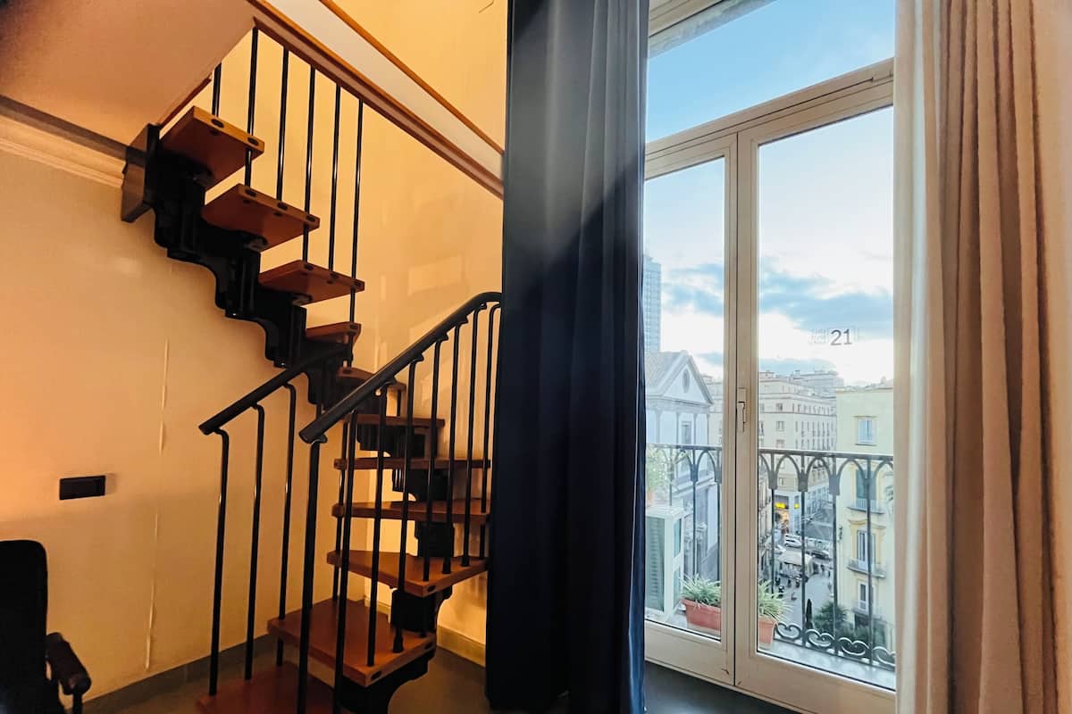 A staircase with wooden steps and black railings, leading to a balcony with a view of buildings and a clear sky.
