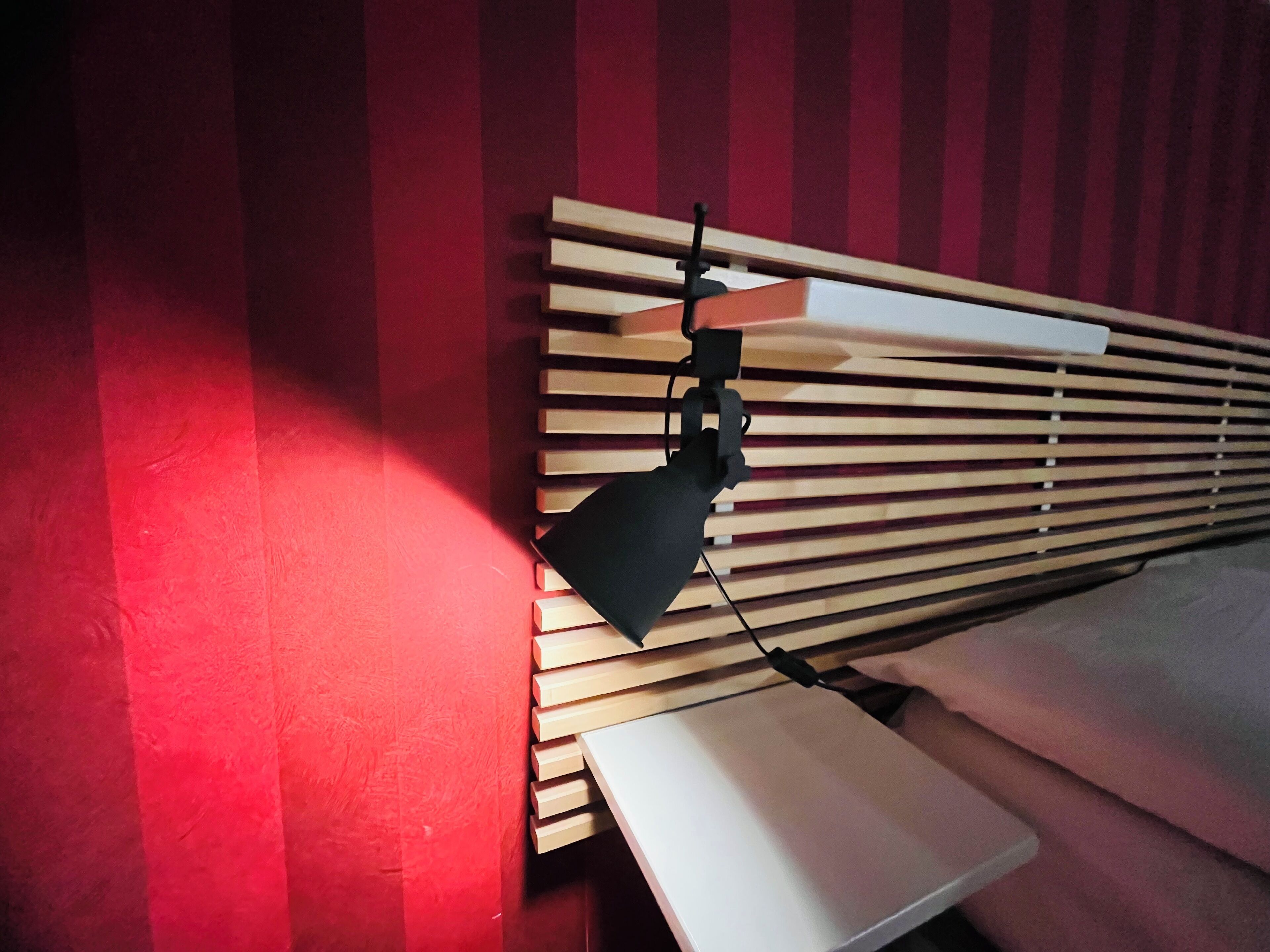 A room with a red striped wall, a wooden slatted headboard, and a white pillow.