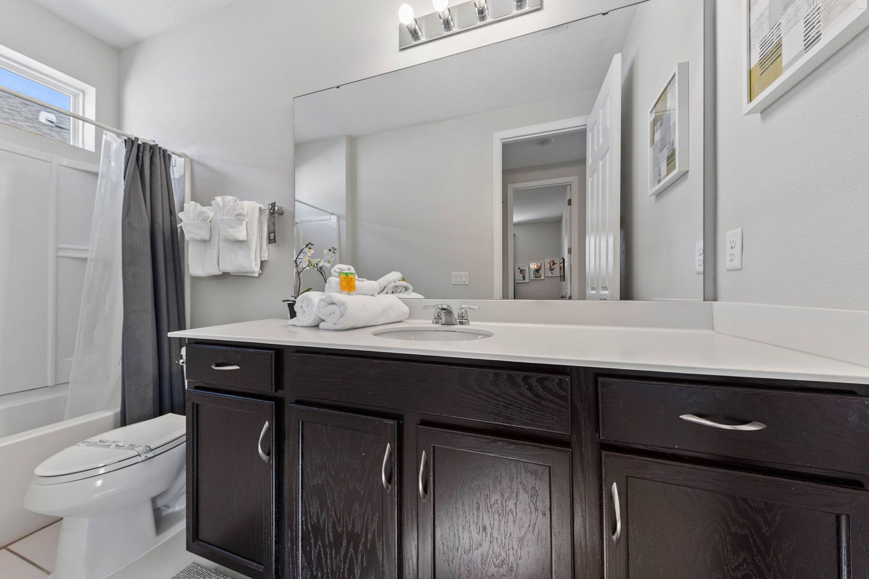 A modern bathroom with a dark wood vanity, white sink, and a large mirror.