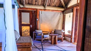 A cozy room with a wooden ceiling, a bed with a canopy, a small table, and two chairs. - SAMBURU ELEPHANT LODGE (Samburu)