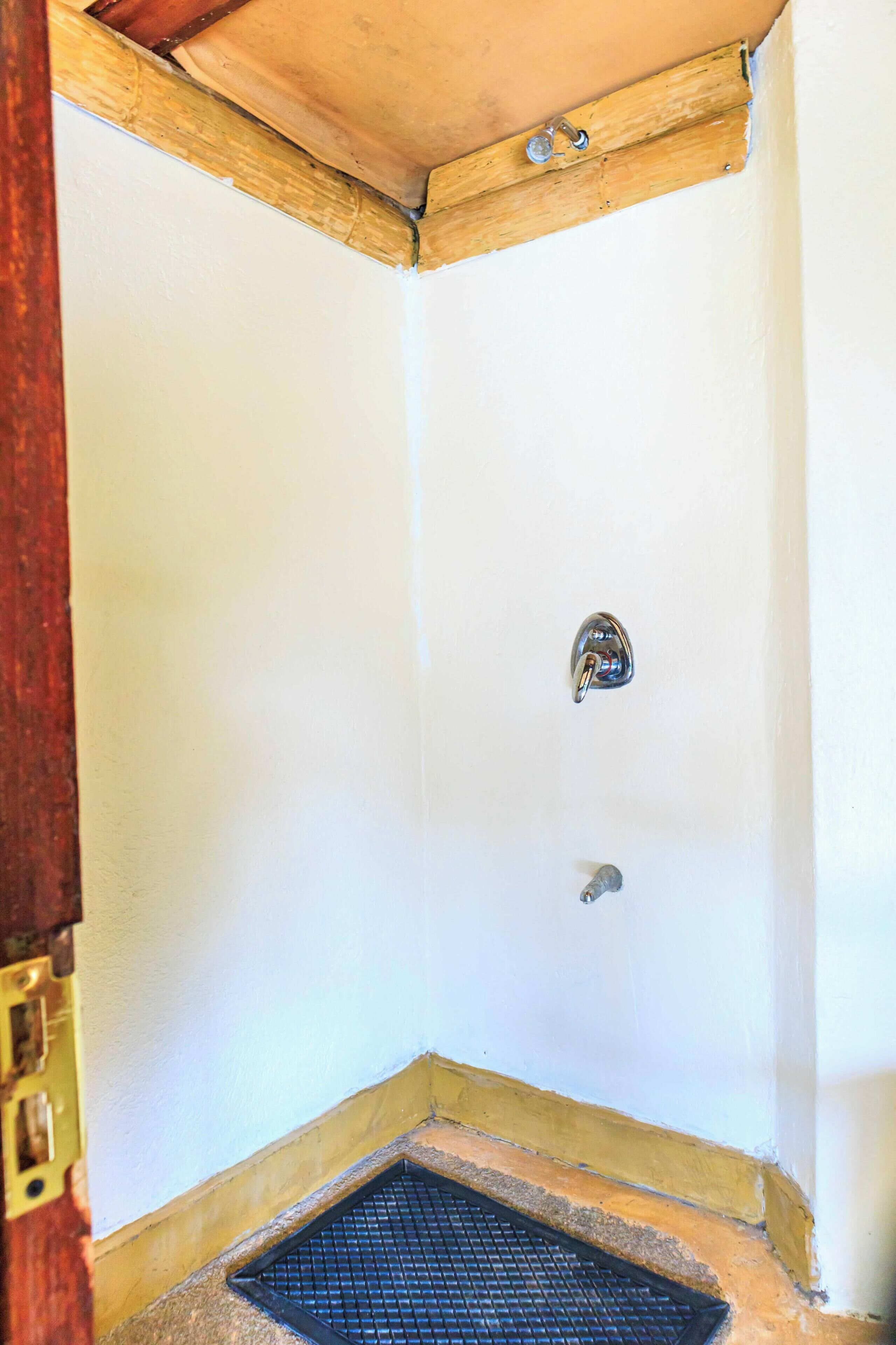 Ducha en esquina con grifo metálico, desagüe y techo de madera.