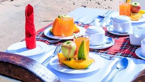 A breakfast setup with plates of fruit, a red napkin, and white cups and bowls on a table outdoors. - SAMBURU ELEPHANT LODGE (Samburu)