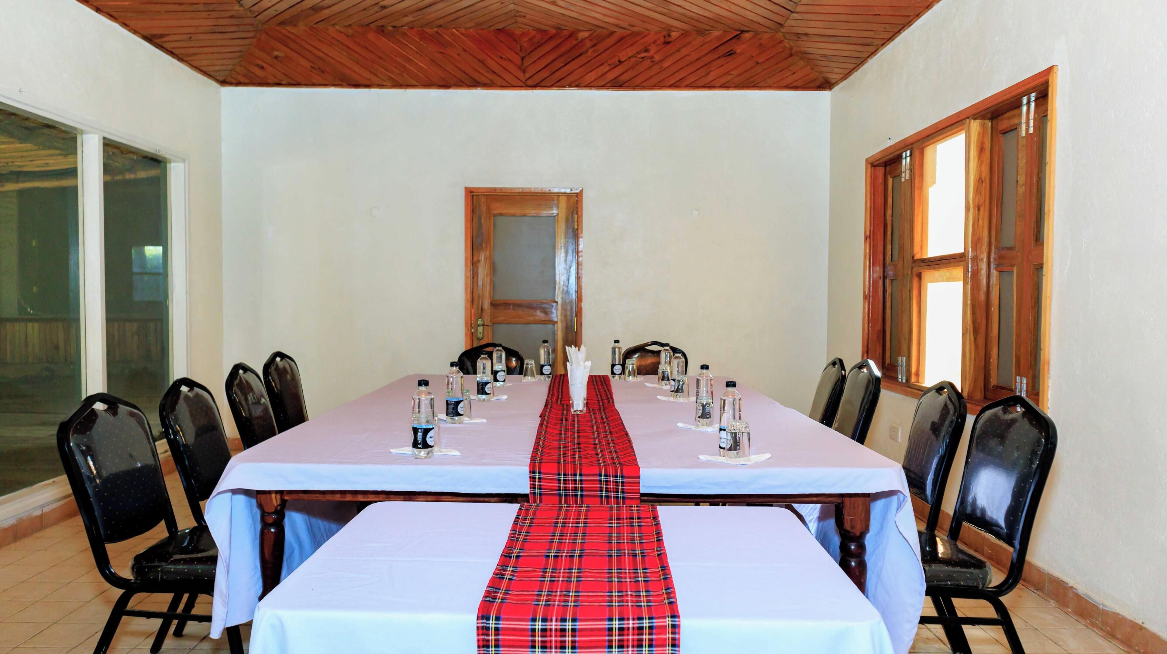 A conference room with a long table, chairs, water bottles, and a red plaid runner.
