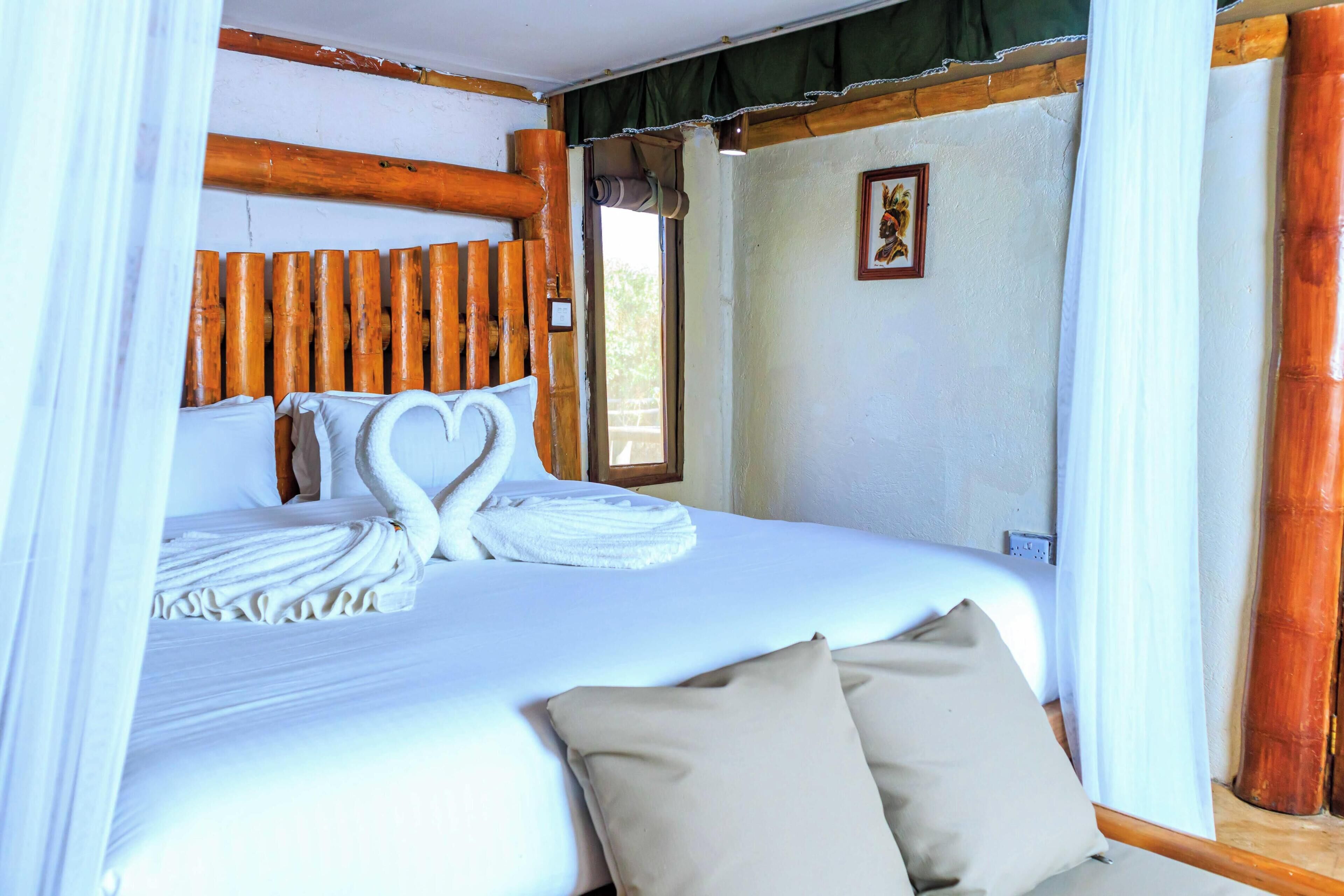 Un lit avec du linge de lit blanc, une décoration en forme de cœur faite avec des serviettes et une tête de lit en bois.