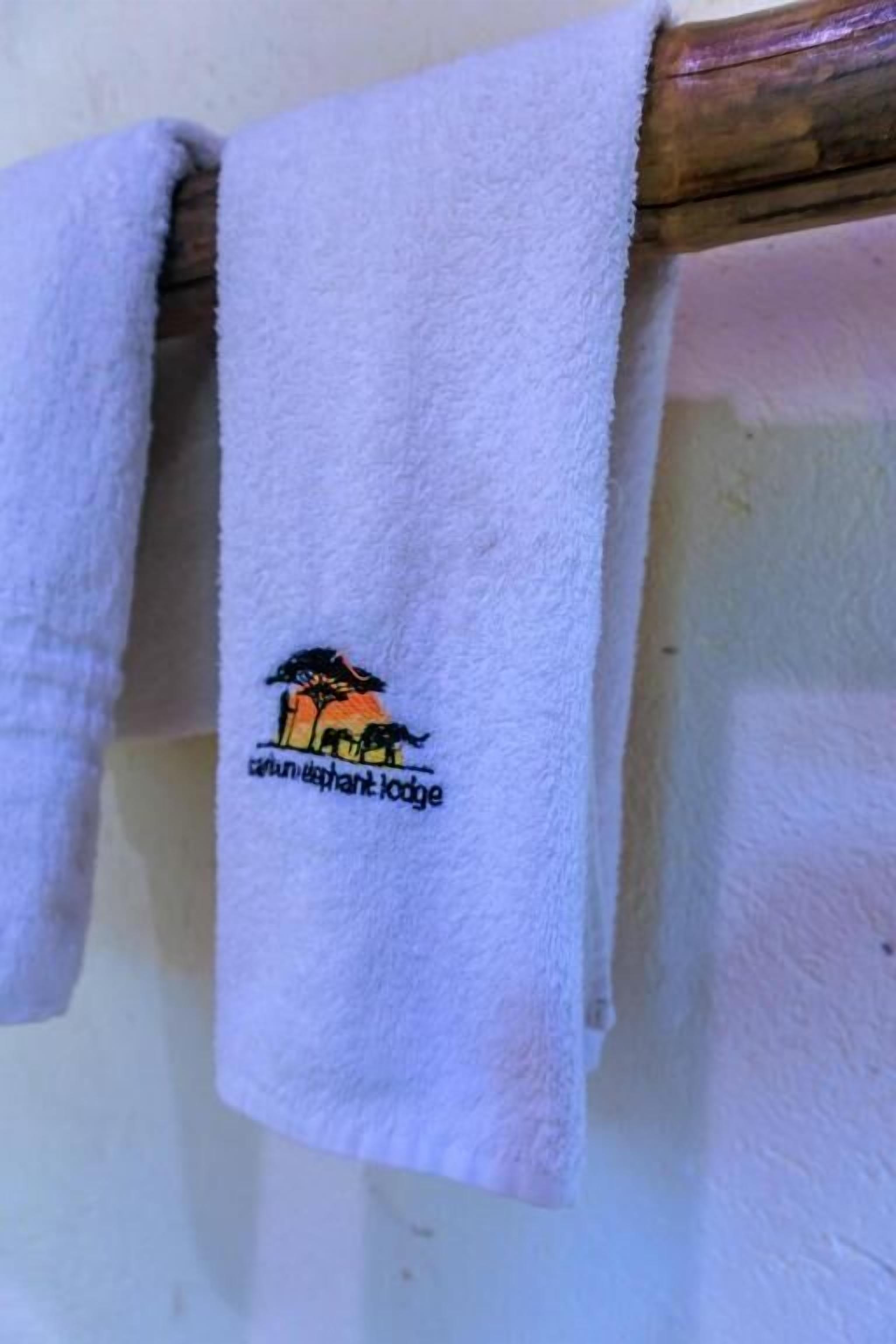 A white towel with an embroidered elephant logo and the text "elephant lodge" hanging on a wooden structure.