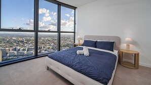 Una camera da letto con un'ampia finestra, un letto, due comodini e vista sulla città.