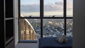 Una stanza con una grande finestra che si affaccia su un panorama urbano, un letto con materasso blu e un orsetto sul letto.